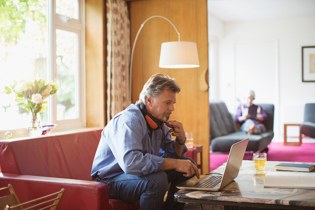 Senior man working at laptop on living room sofa
