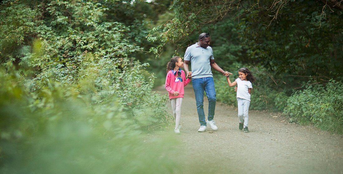 Father and daughters holding hands on path in park