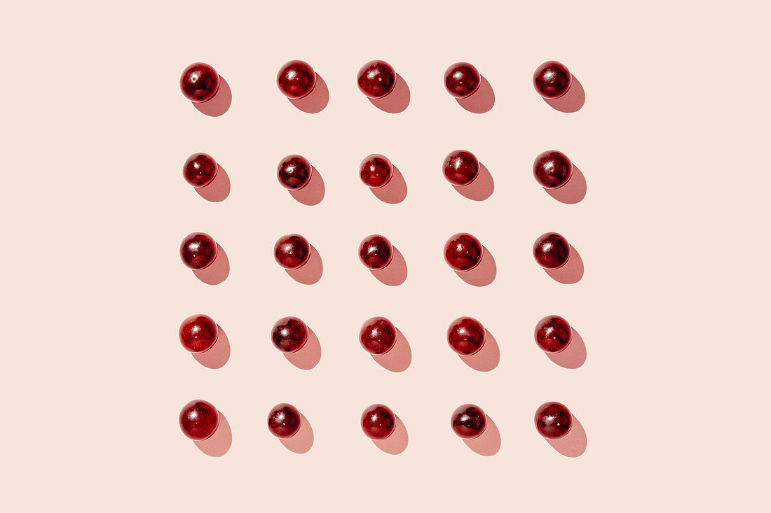 Pattern of fresh red grapes arranged in lines on pink surface in studio