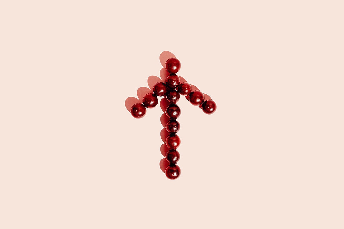 Red grapes arranged in arrow showing direction on pink background