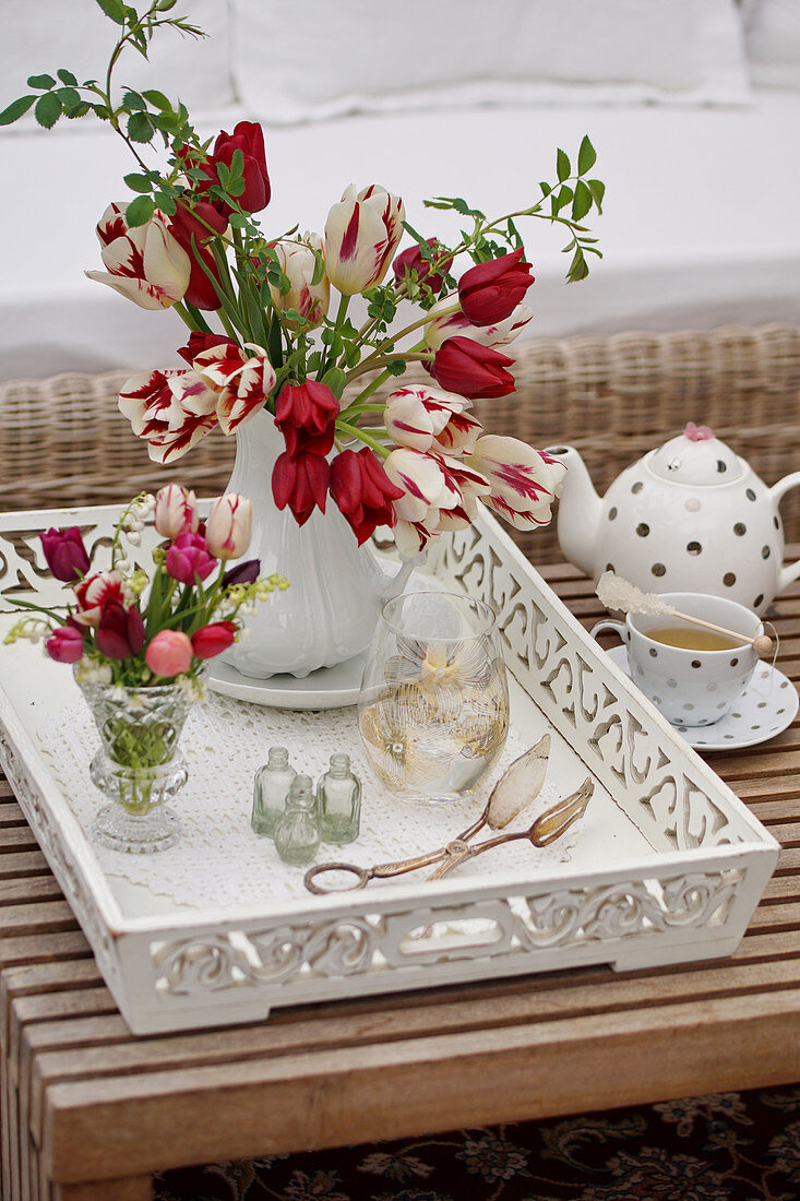 Vase of tulips, wild roses and lily-of-the-valley on white wooden tray