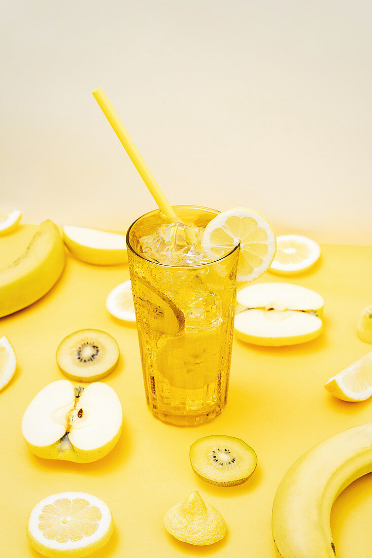 Various fresh fruits arranged on yellow background with glass of cocktail with straw and ice