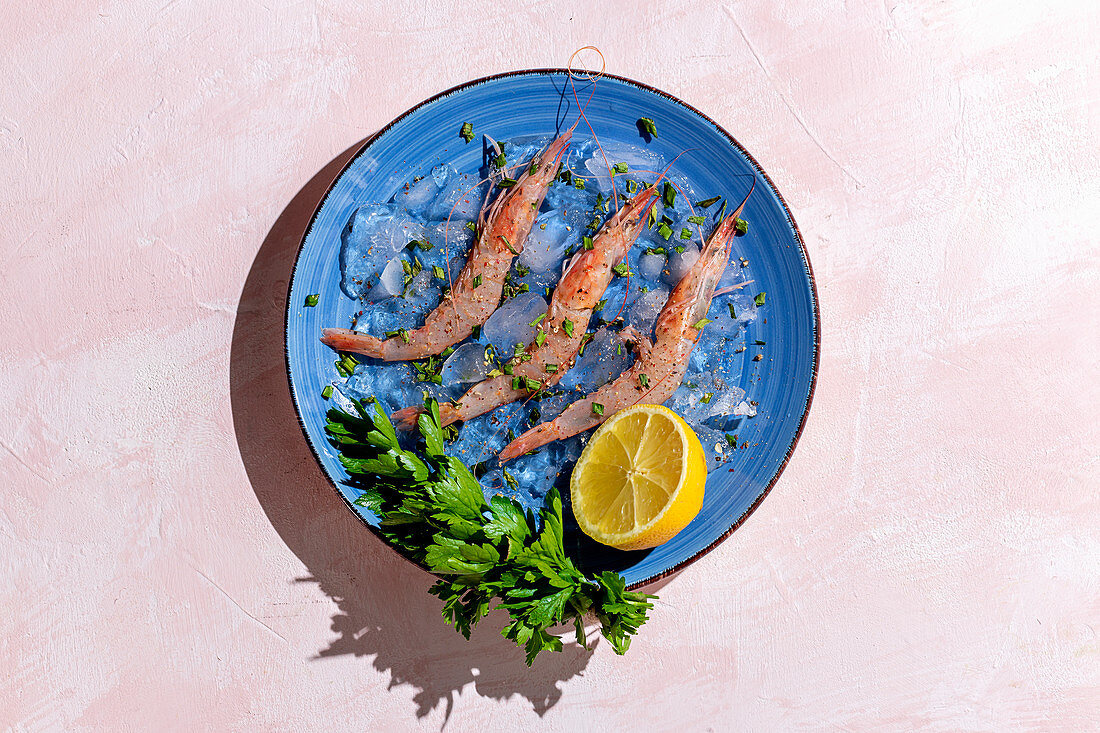 Tasty prawns on blue plate with half of lemon and bunch of fresh parsley on multicolored background