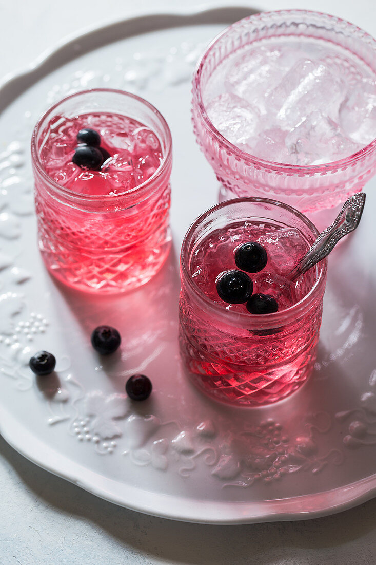 Healthy pink beverage decorated with fresh blueberries, bowl with ice cubes