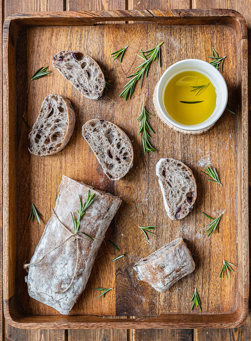 Italian ciabatta bread served on wooden tray with pot of olive oil and fresh rosemary