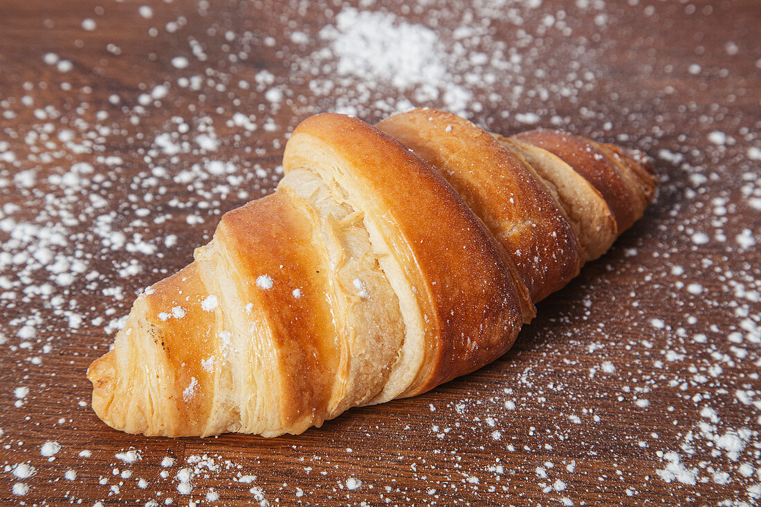 Croissant with golden crust on wooden table with sprinkled with glace sugar