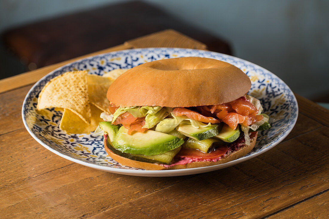 Lachsbagel mit Tomatentartar, Avocado und Pickles auf Holztisch