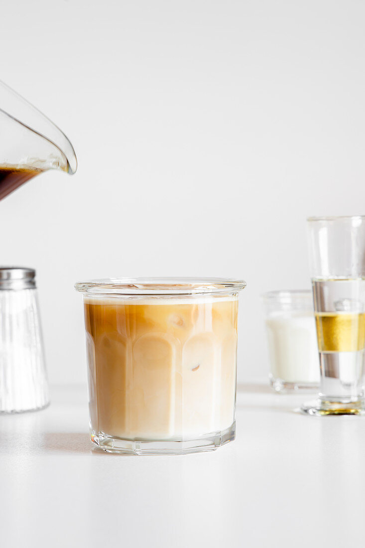Iced coffee latte served in glass cup on white table with cup of milk and glassware