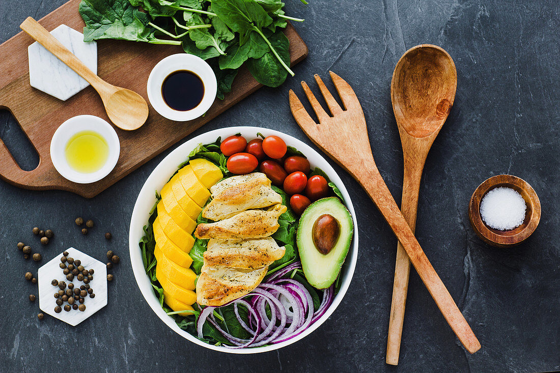 Fried chicken, mango, cherry tomatoes, avocado and onion on spinach leaves