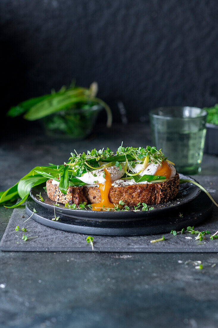 Open faced sandwich topped with wild garlic and an egg with a broken yolk