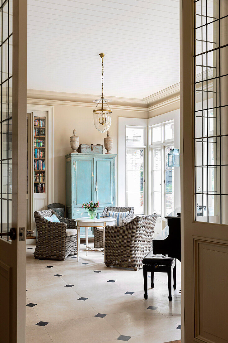 Blick in den Salon mit rundem Tisch, Rattansesseln und blauem Schrank, Bodenfliesen aus Kalkstein