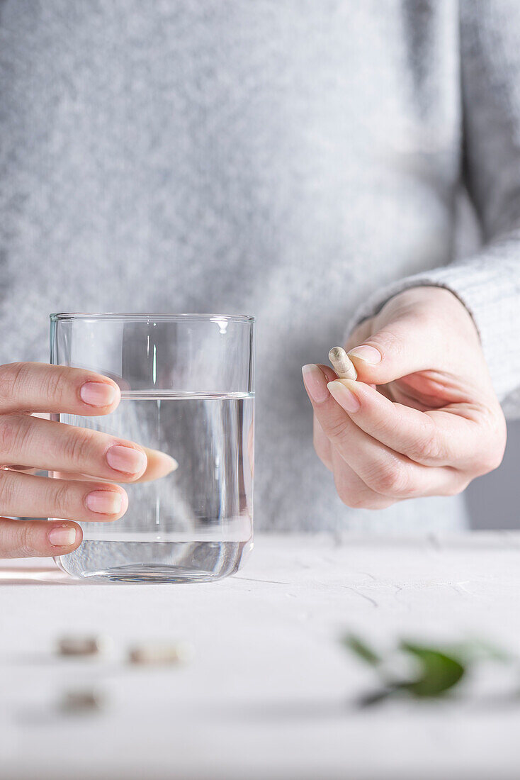 Hände halten Supplement und ein Glas Wasser