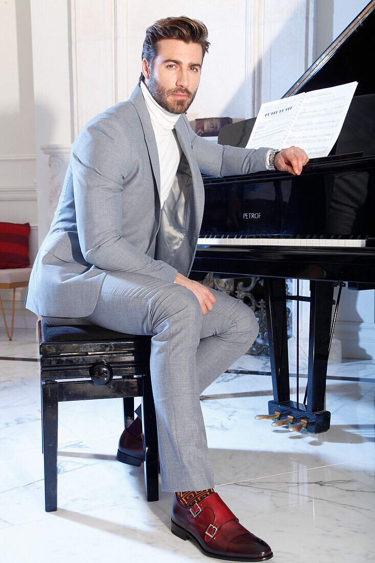 Young man with a beard in a light gray suit sits at the piano