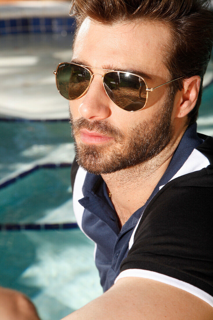 Junger Mann mit Bart und Sonnenbrille in Polo-Shirt am Pool