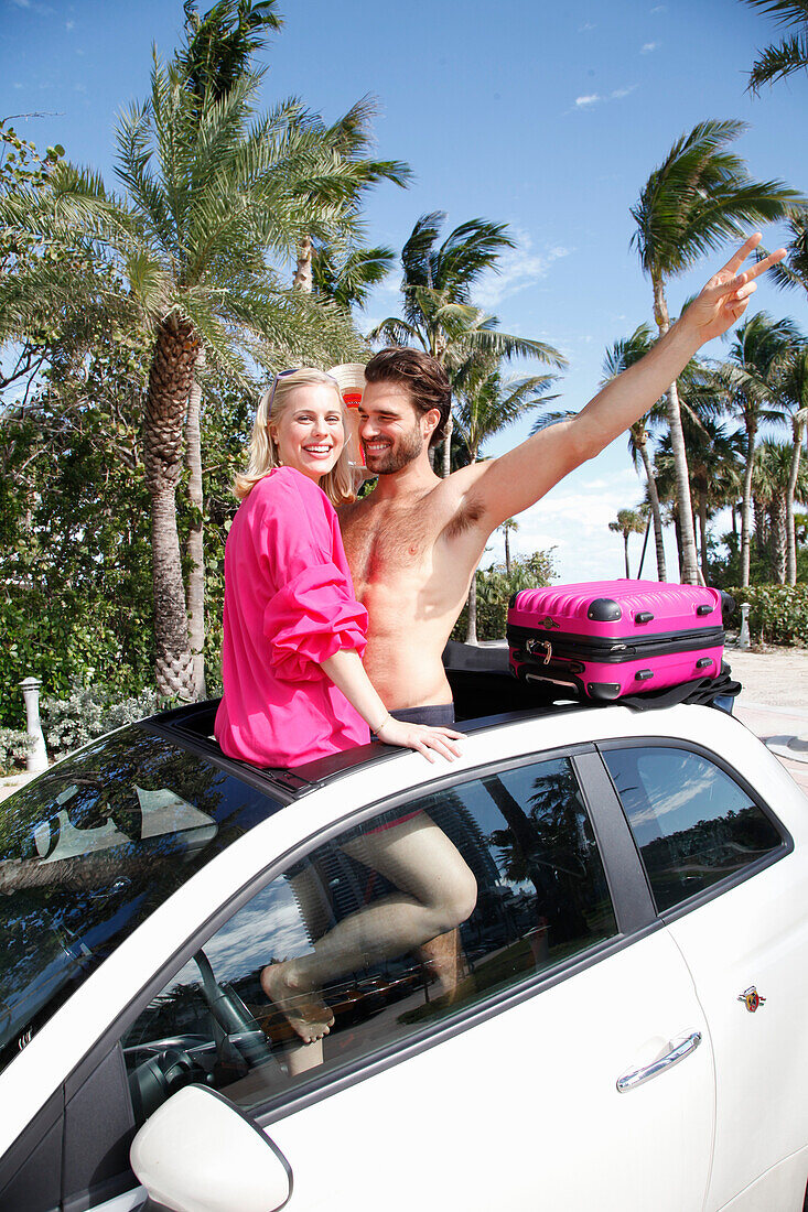 Cheerful couple in holiday spirit are standing in the roof window opening of a car