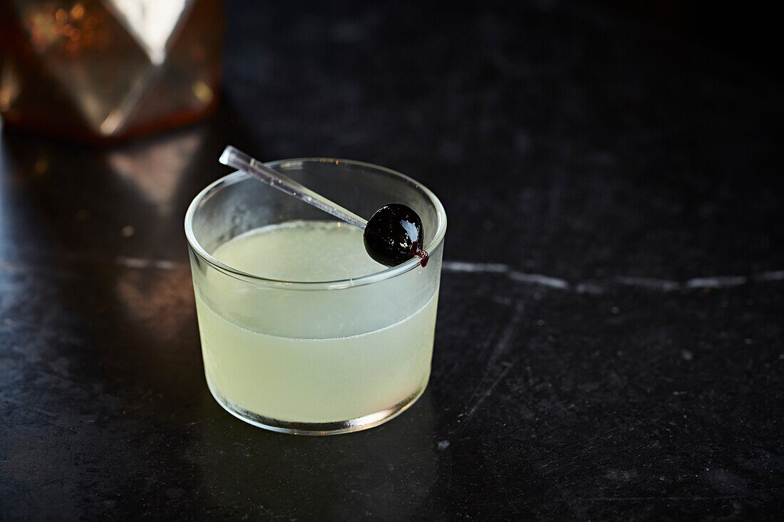 A lime cocktail garnished with an Amarena cherry