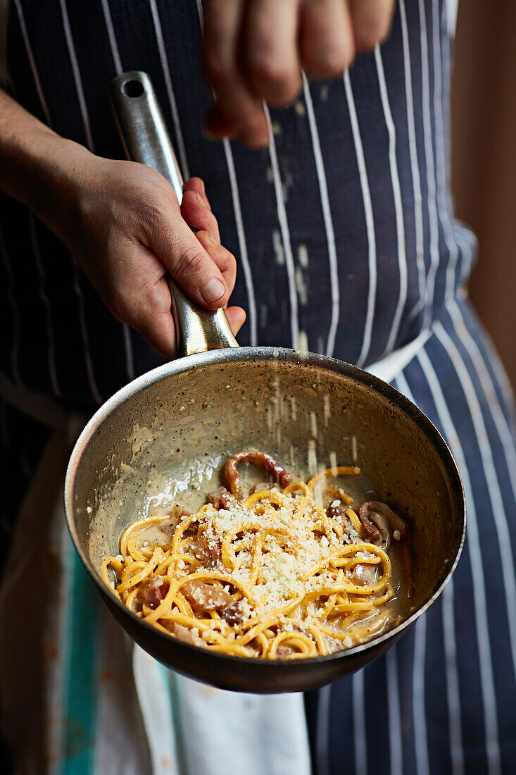 A chef sprinkling Parmesan cheese over pasta