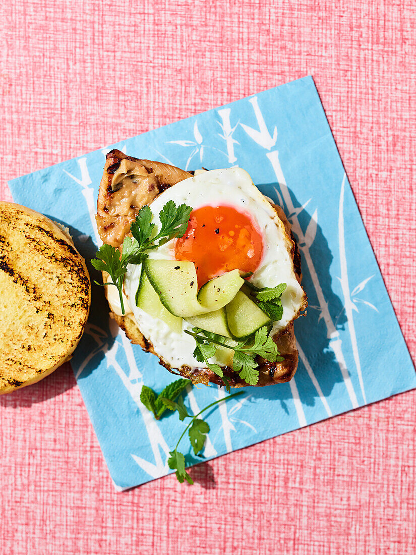 Gegrillter Saté-Hähnchen-Burger mit Spiegelei und gepickelter Gurke