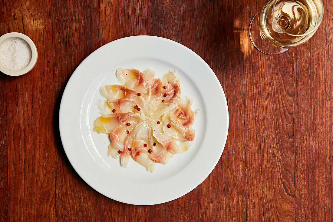 Fisch-Carpaccio mit roten Pfefferkörnern serviert mit einem Glas Weißwein