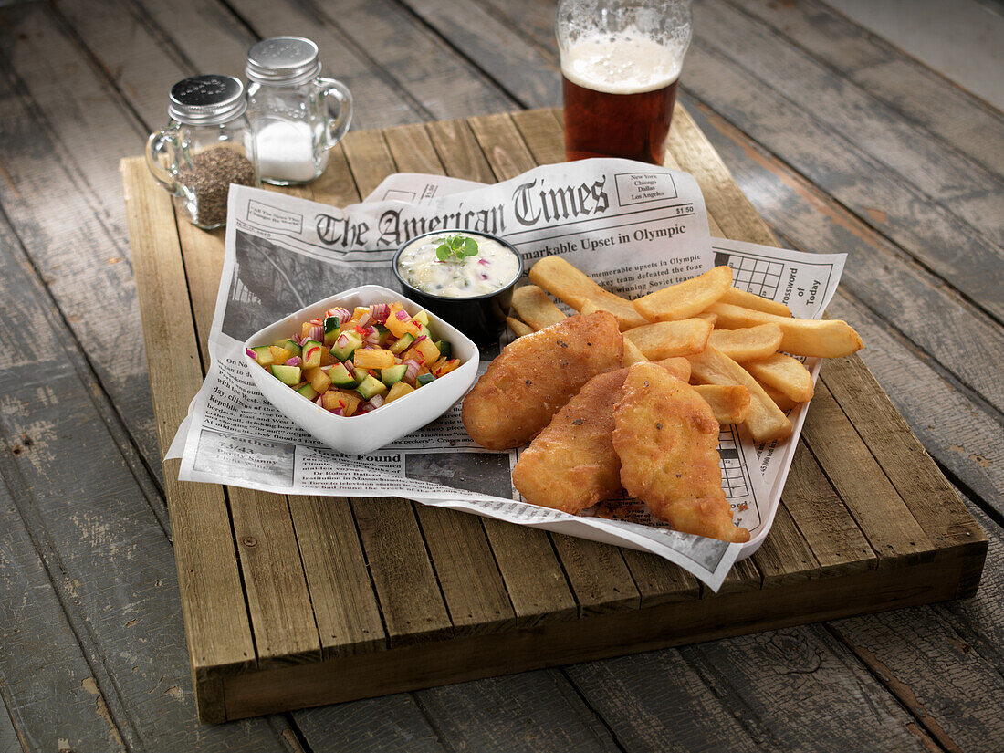 Fish and chips with a vegetable salad and a dip on newspaper