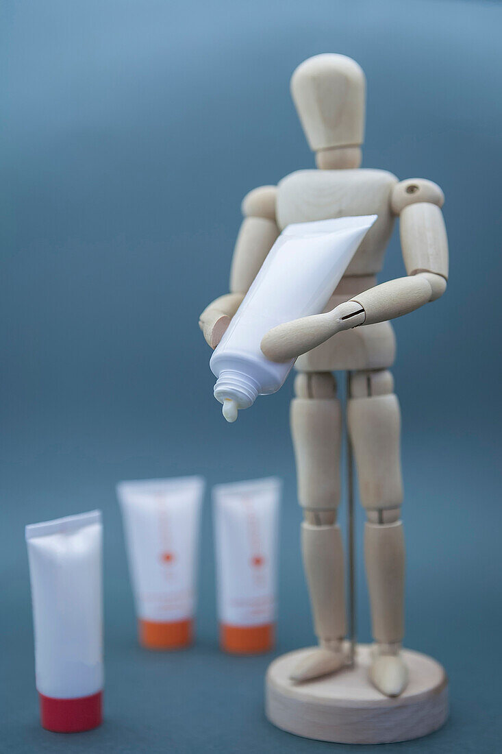 Wooden mannequin holding a tube of lotion