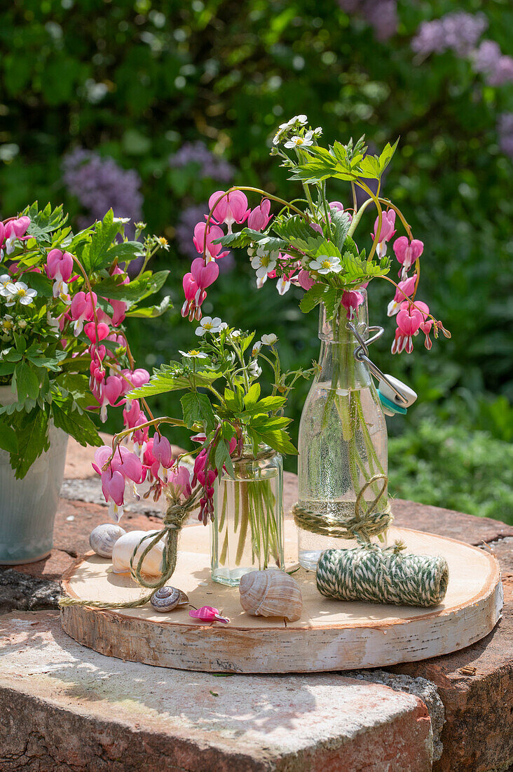 Tränendes Herz (Dicentra Spectabilis), rosa Blüten in Vasen und Erdbeerblüten, close-up