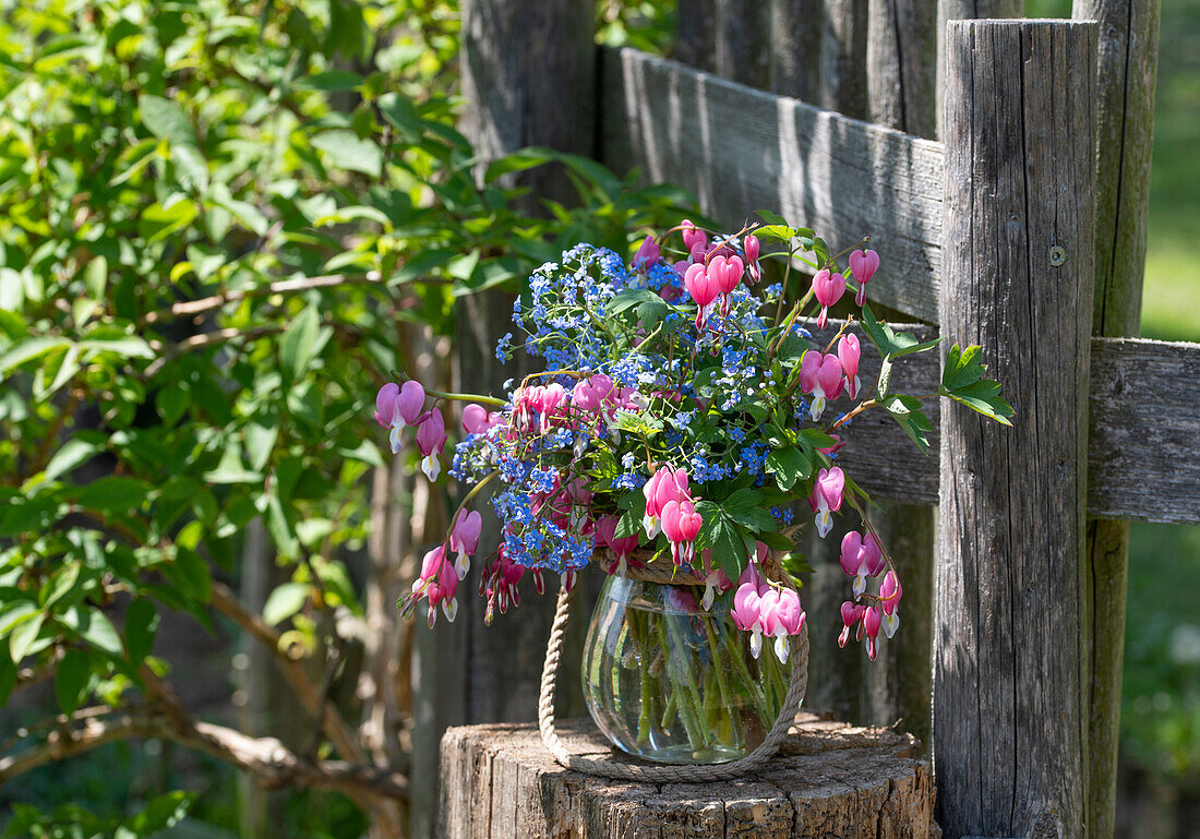 Blumenstrauß Tränendes Herz (Dicentra Spectabilis) und Kaukasus-Vergissmeinnicht (Myosotis) auf Baumstumpf