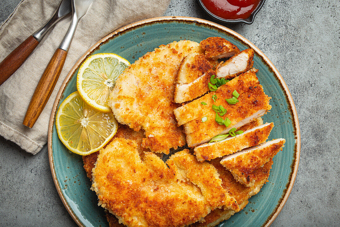 Crispy panko breaded fried chicken fillet with green salad and lemon