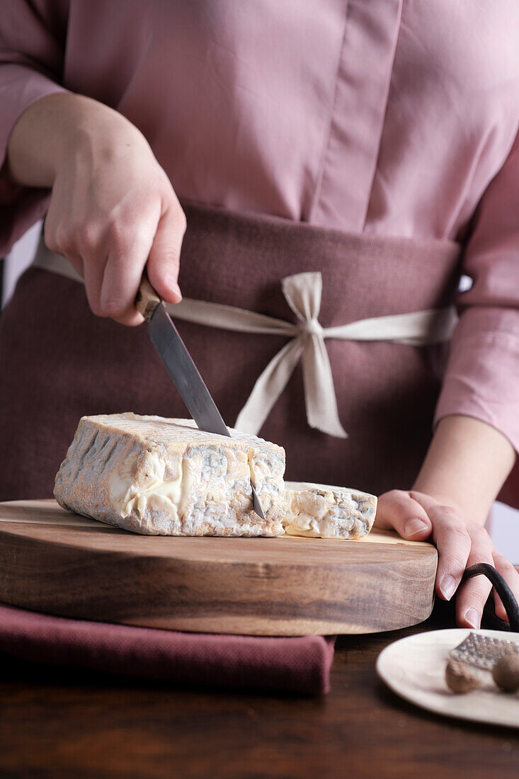 Taleggio-Käse auf Holzbrett schneiden