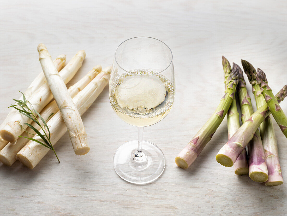 White and green asparagus in between a glass of white wine