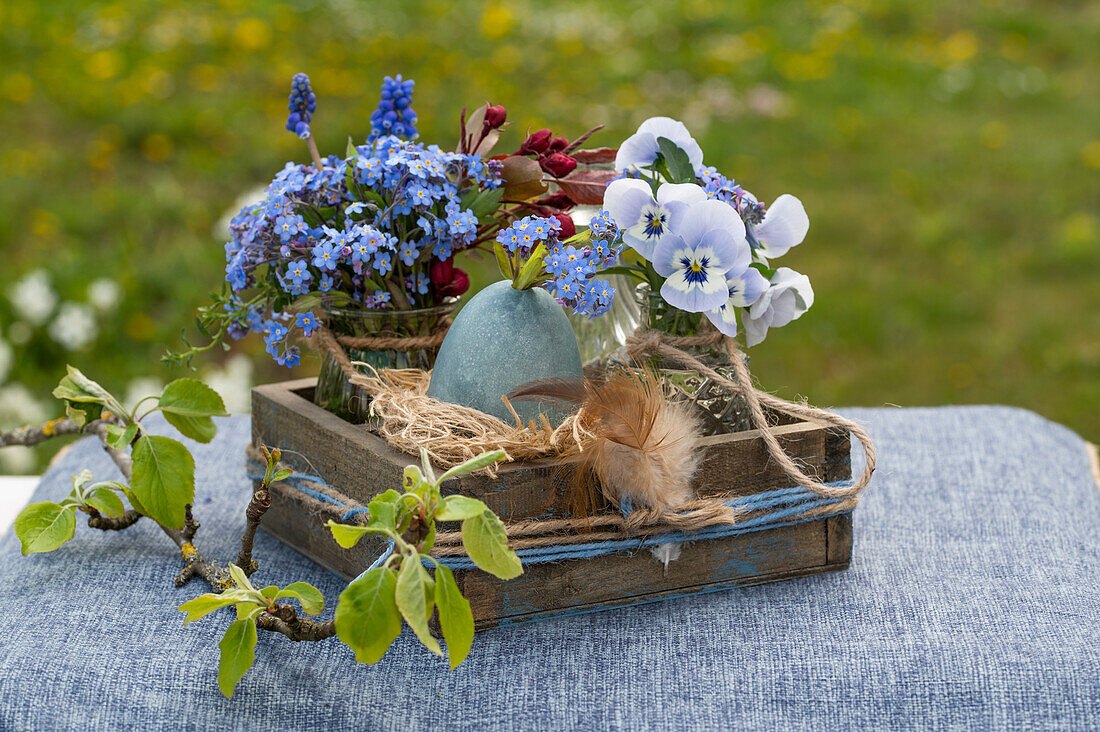 Osternest mit Ei, Feder, Traubenhyazinthe (Muscari), Vergissmeinnicht, Hornveilchen (Viola Cornuta) und Zweig