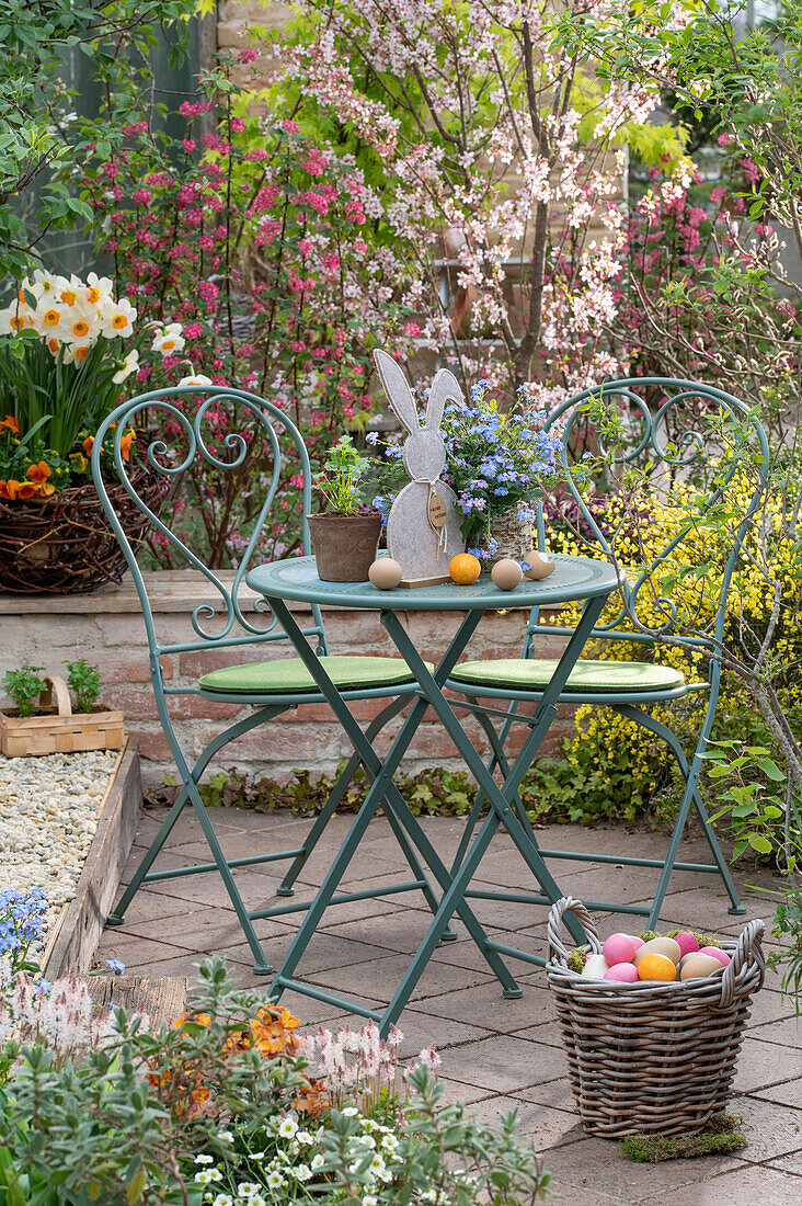 Colourful Easter eggs in a basket, rabbit figurine, forget-me-nots, daffodils and flowering shrubs, blood currant (Ribes sanguineum)