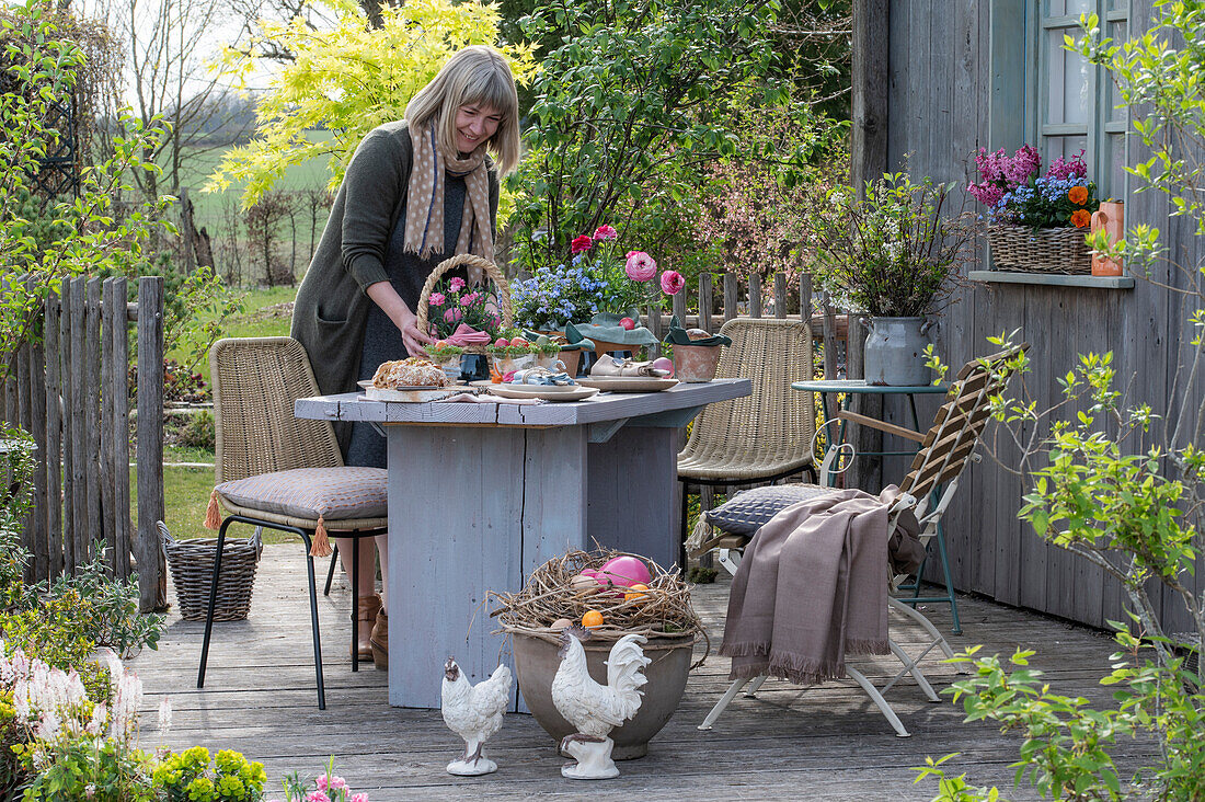 Woman decorates garden table with Easter decoration, Easter nest with eggs and flower pots