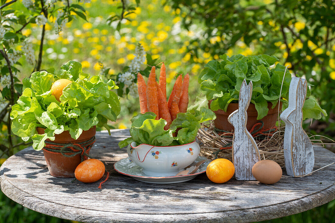 Green lettuce with carrots in a soup bowl and rabbit figurines, Easter decoration on the garden table