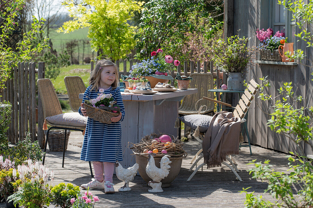 Kleines Mädchen am gedeckten Tisch auf der Terrasse mit Osterdekoration