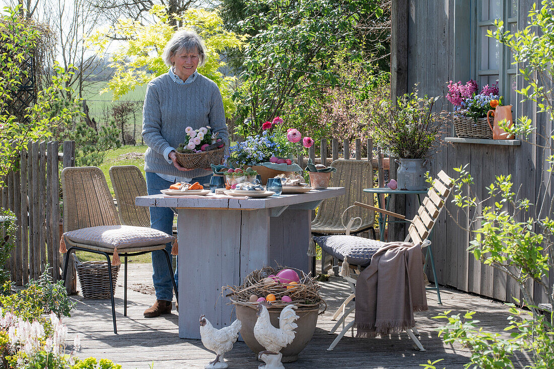 Frau deckt Tisch mit Osterdekoration auf der Terrasse