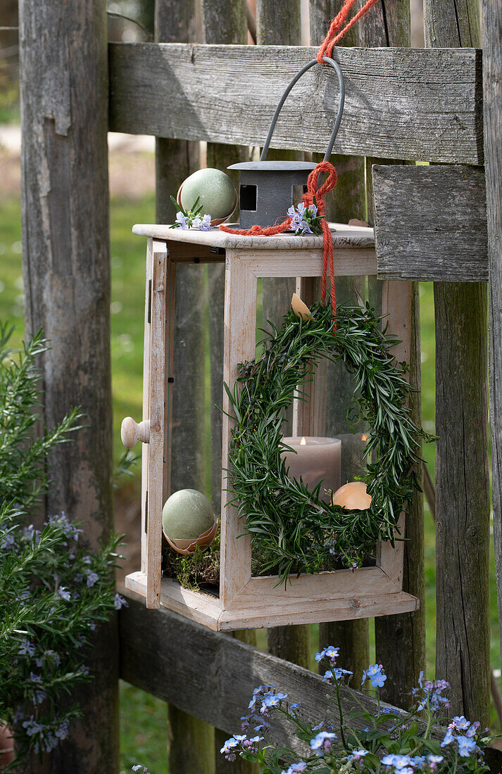 Easter decoration in the garden, Easter wreath and eggs hanging from a lantern on a fence, forget-me-not (Myosotis)