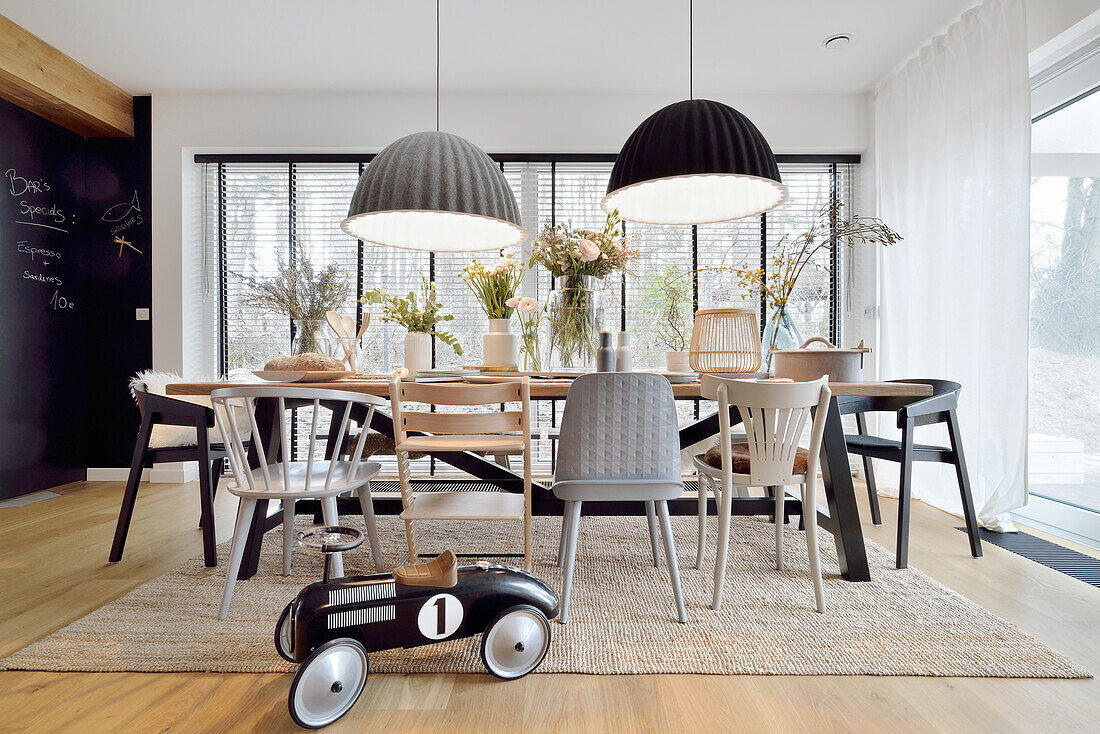 Long dining table with various chairs, above hanging lamps in front of glazing in open living area