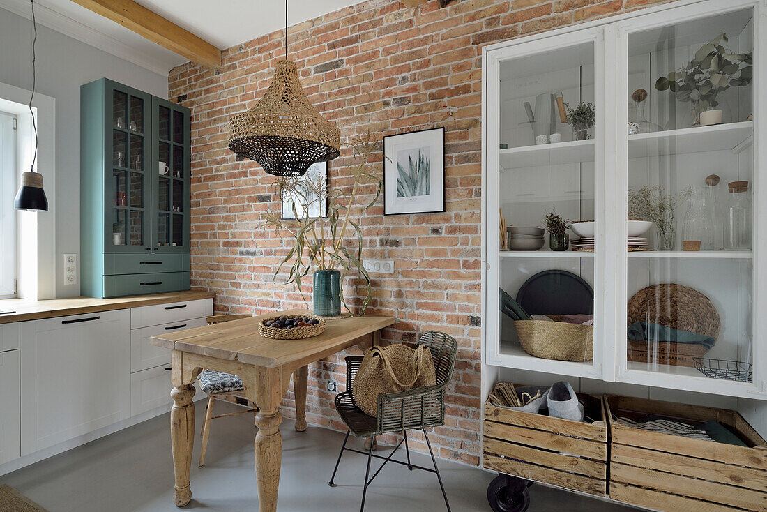 Weiße Vitrinenschrank und Holztisch in Küche mit Backsteinwand