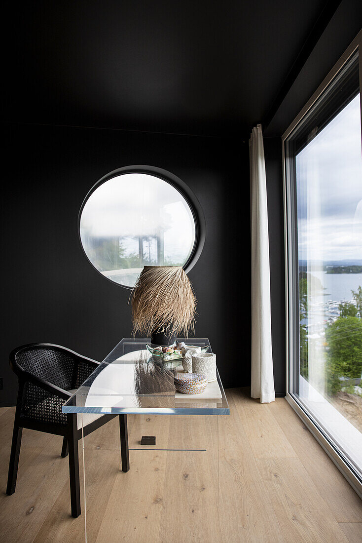 Eleganter Schreibtisch aus Plexiglas und Stuhl im Zimmer mit schwarzen Wänden und raumhoher Verglasung