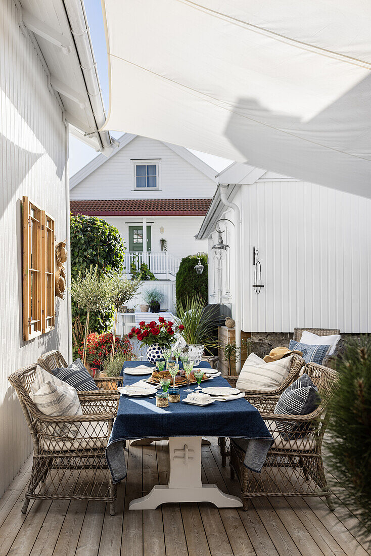 Gedeckter Tisch mit Rattanstühlen auf Holzterrasse mit Sonnensegel