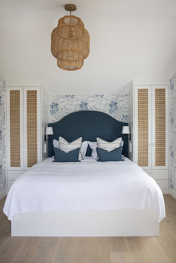 Double bed in bright, light-flooded bedroom with blue and white wallpaper