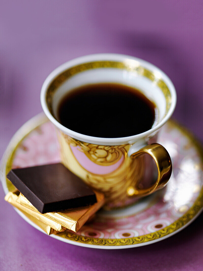 Tasse Kaffee mit Schokoladentäffelchen auf Untertasse