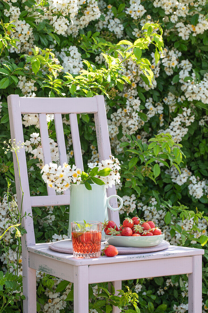 Fresh strawberries, drink and bouquet on wooden chair in garden