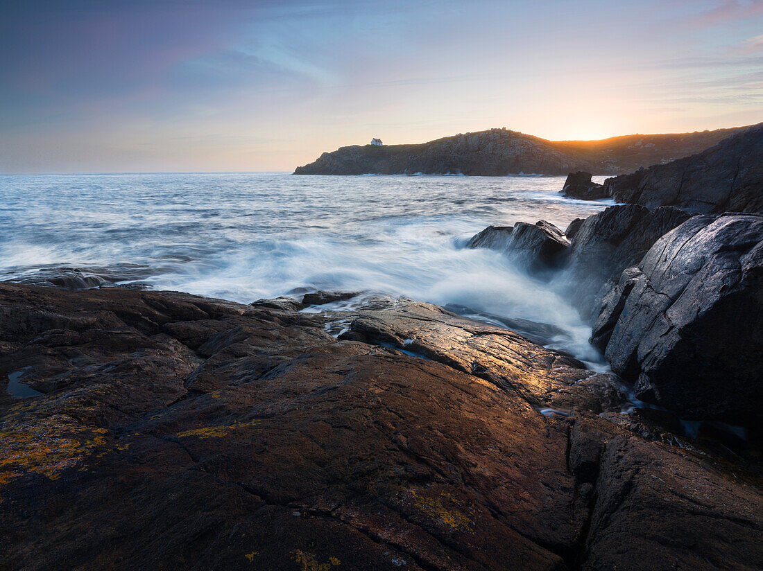 Sonnenaufgang über einer Bucht mit Wellen, die durch die Kamera kommen, Bretagne, Frankreich, Europa
