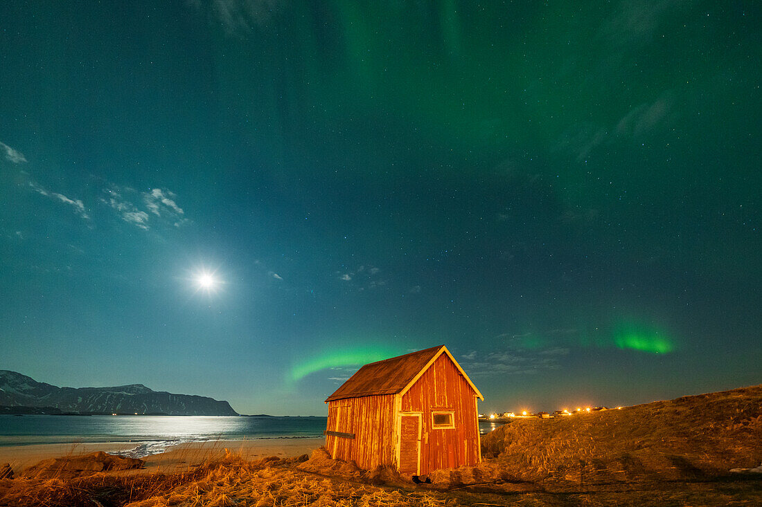 Red wood cabin on sand beach lit by moon during the Aurora Borealis (Northern Lights), Ramberg, Nordland county, Lofoten Islands, Norway, Scandinavia, Europe