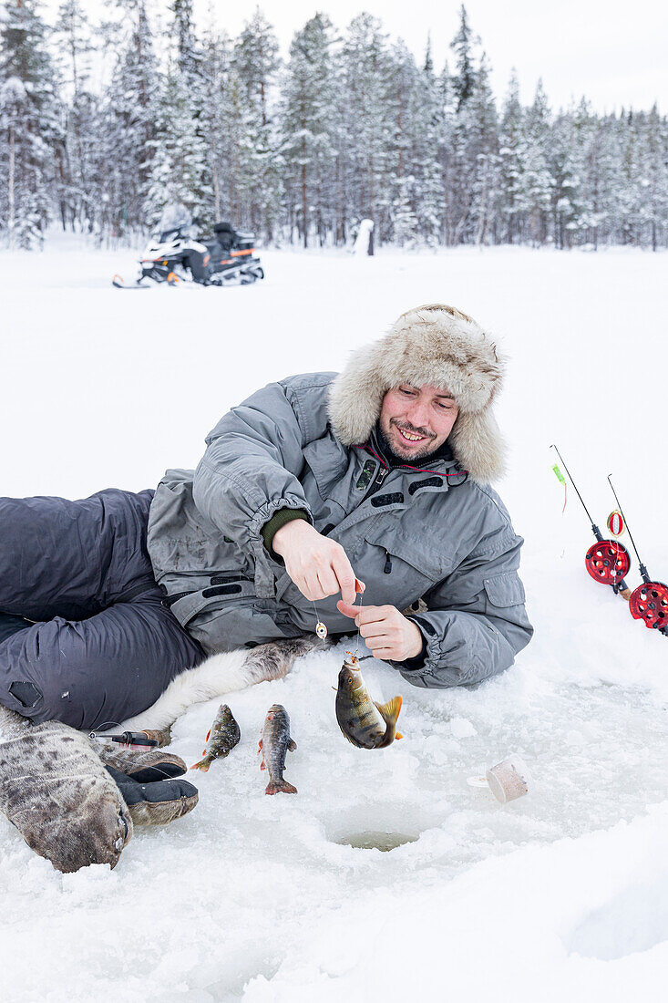 Fröhlicher Mann, der seinen Fischfang aus dem Eisloch aufhebt, Lappland, Schweden, Skandinavien, Europa