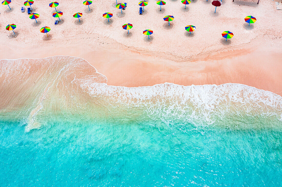 Mehrfarbige Sonnenschirme am tropischen Strand, umspült von den Wellen des Karibischen Meeres, Luftaufnahme, Antigua, Westindien, Karibik, Mittelamerika