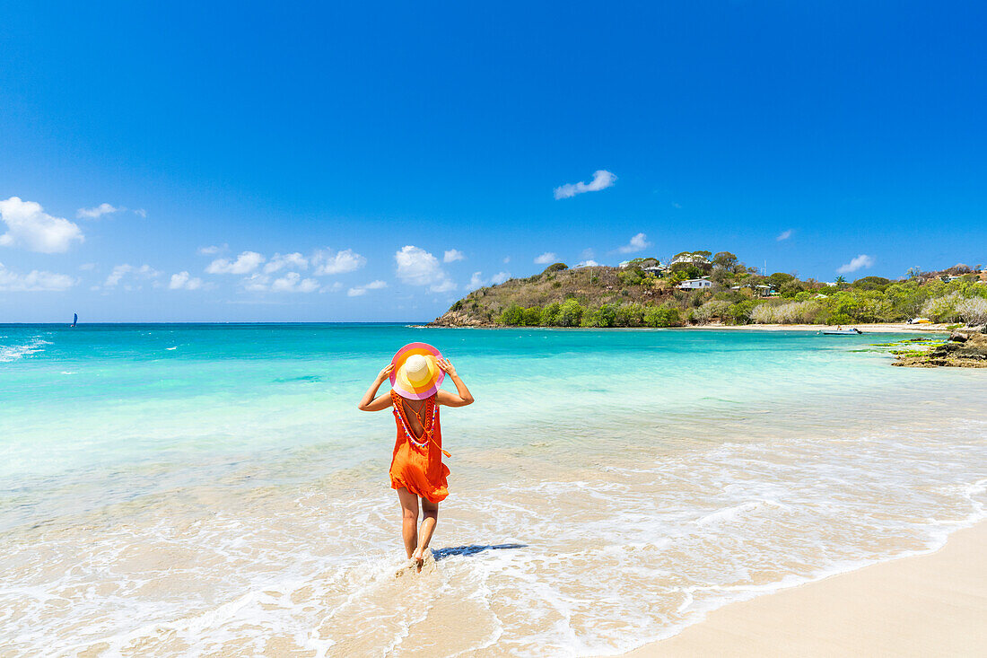 Schöne Frau mit orangefarbenem Kleid und Strohhut an einem tropischen Strand, Antigua, Westindien, Karibik, Mittelamerika