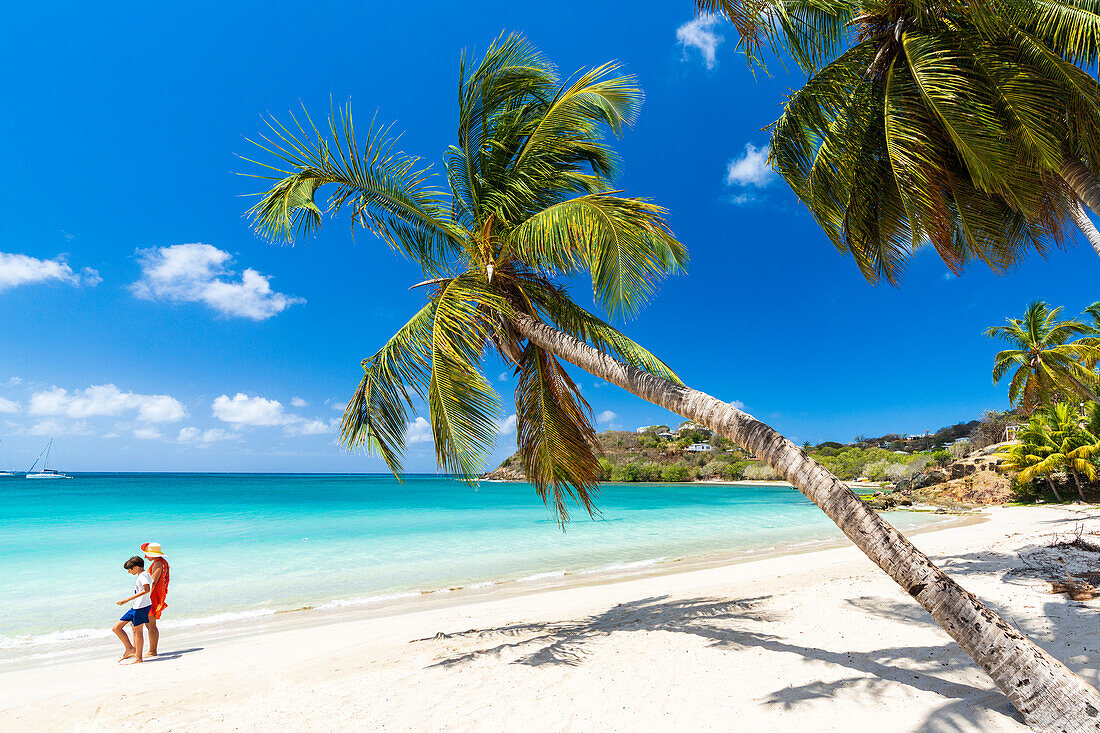 Cheerful little boy with mother walking on idyllic palm fringed beach, Antigua, Leeward Islands, West Indies, Caribbean, Central America